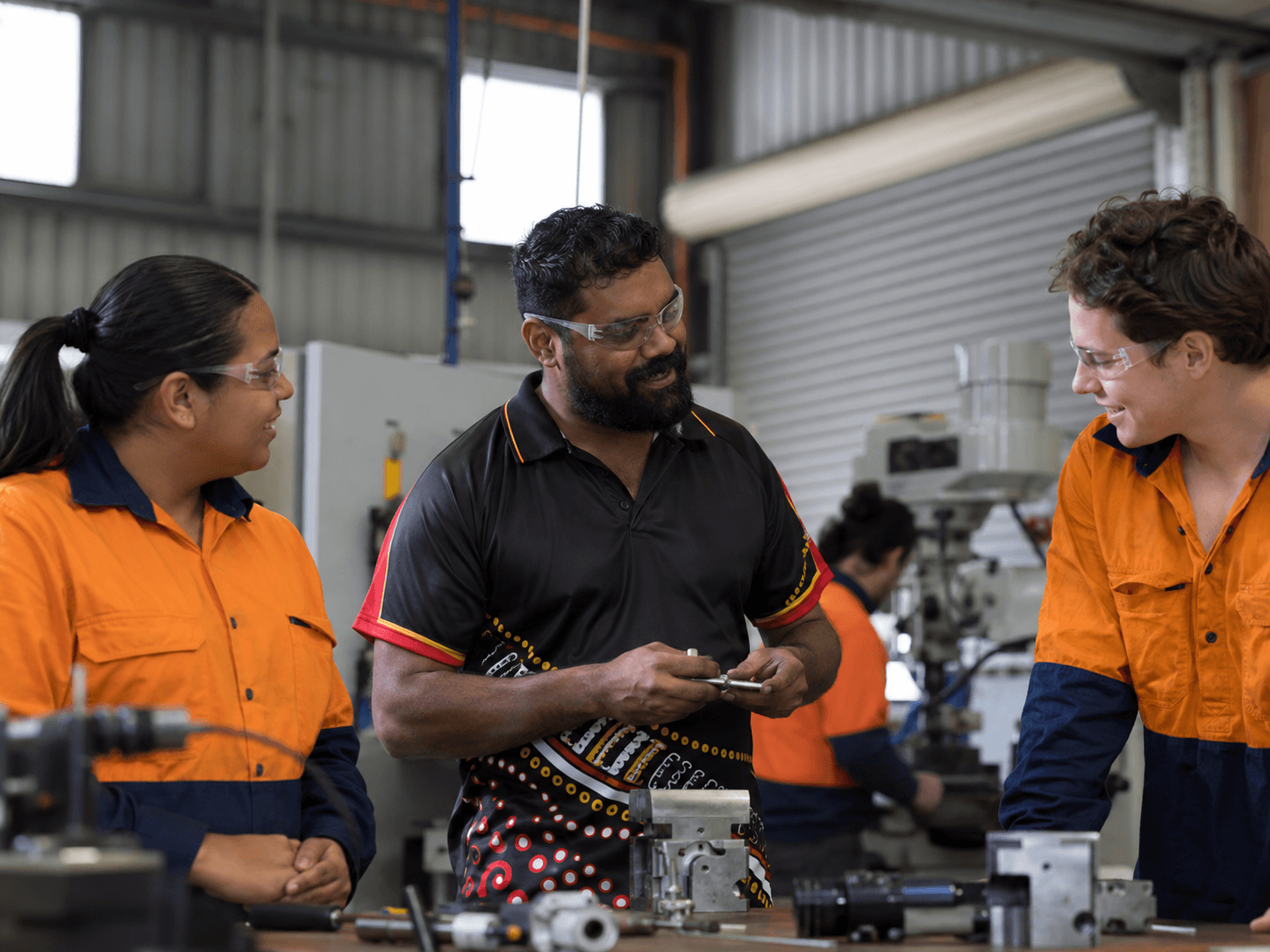 Three workshop colleagues talking over a machined part at a workbench