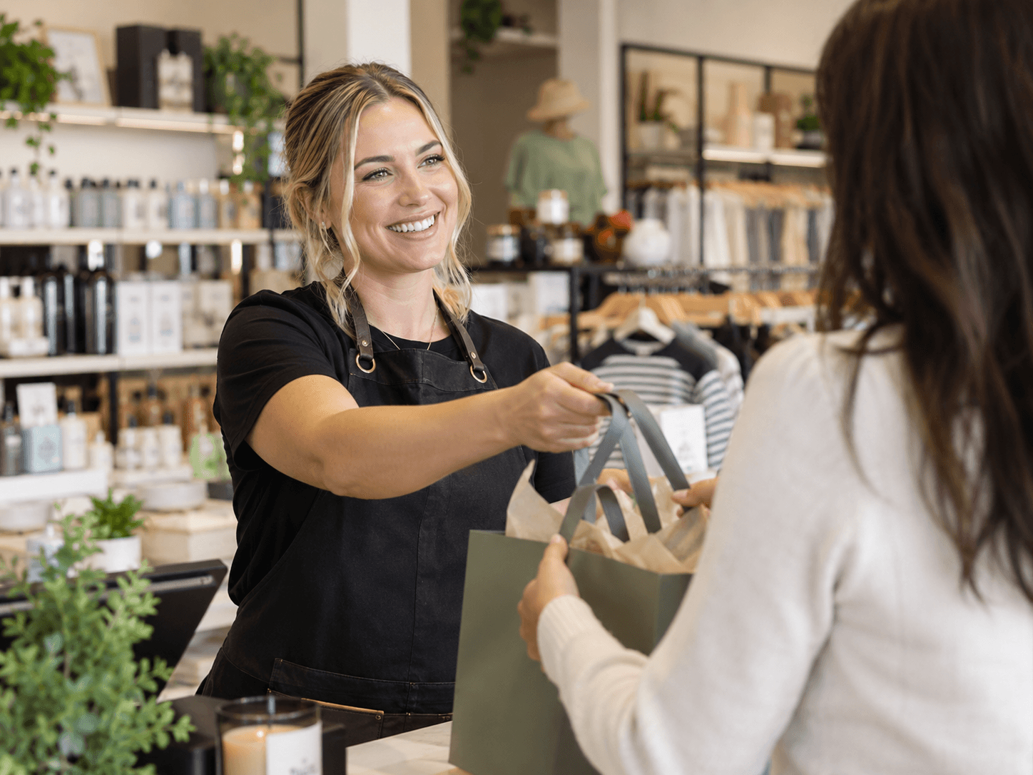 A retail assistant smiling as she hands a customer their bag at the counter
