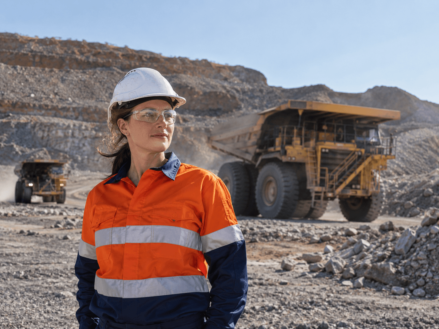 A mine worker in high-visibility workwear with haul trucks in an open pit behind her